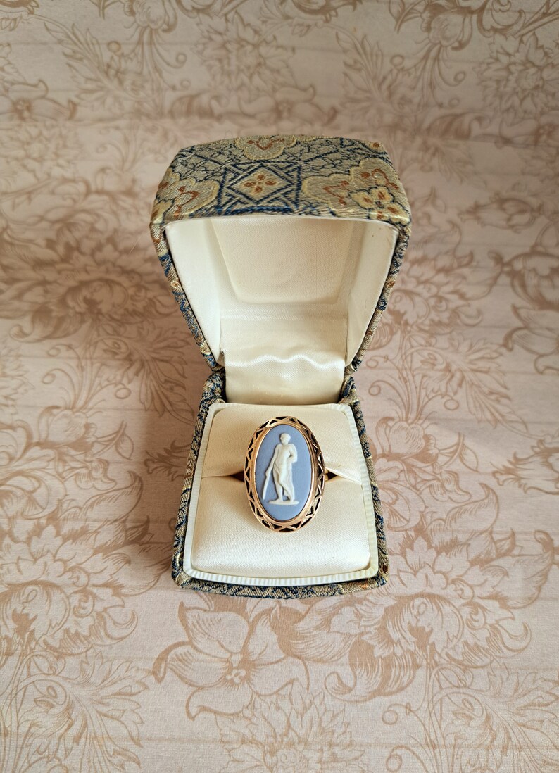Pu&ograve; includere: Un anello cammeo blu con una montatura in oro, che presenta un cammeo bianco di una donna con un vestito lungo, in una piccola scatola di velluto.