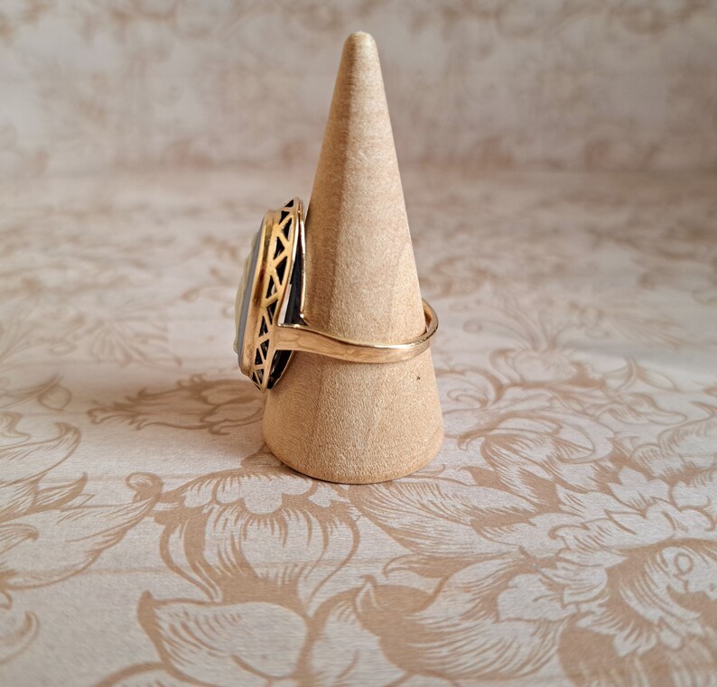 Pu&ograve; includere: Un anello d'oro con una pietra ovale bianca e nera incastonata in un design a filigrana d'oro. L'anello &egrave; esposto su un porta anelli in legno.