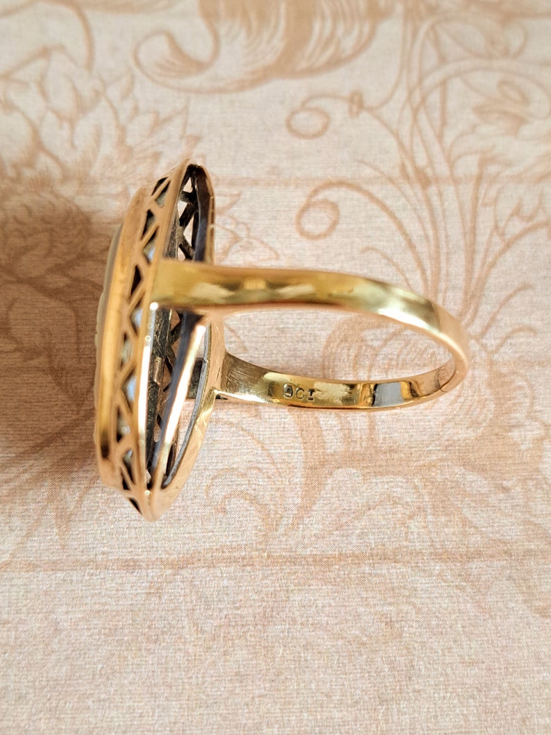 Pu&ograve; includere: Un anello d'oro con una grande pietra ovale incastonata in un design delicato e intricato. L'anello &egrave; contrassegnato "585" sulla fascia interna.
