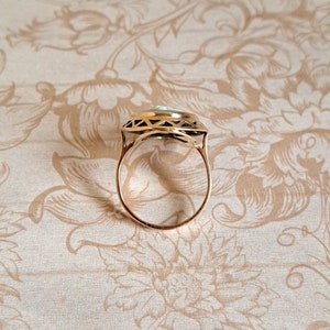 Pu&ograve; includere: Un anello d'oro con una pietra bianca incastonata in un design geometrico.