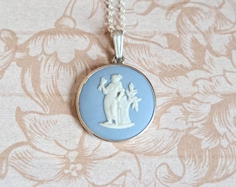 Può includere: Una collana con catena d'argento con un ciondolo a cammeo blu e bianco raffigurante una donna che tiene un ramo. Il cammeo è incastonato in una cornice d'argento.