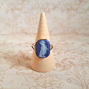 K&ouml;nnte beinhalten: Ein goldener Ring mit einem blauen Kamee, der eine Frau in einem wei&szlig;en Kleid zeigt.