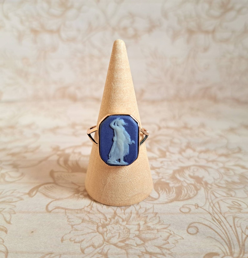 K&ouml;nnte beinhalten: Ein goldener Ring mit einem blauen Kamee, der eine Frau in einem wei&szlig;en Kleid zeigt.