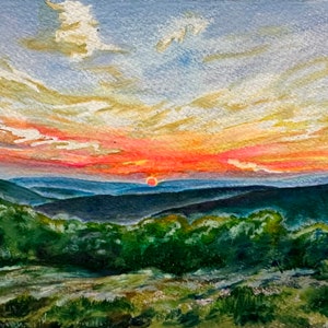 Könnte beinhalten: Ein Aquarellgemälde eines Sonnenuntergangs über einem Gebirge. Der Himmel ist eine Mischung aus Rosa, Orange und Gelb mit Wolken im Hintergrund. Die Sonne geht hinter den Bergen unter, die eine dunkelblaue Farbe haben. Der Vordergrund ist ein Feld mit grünem Gras.