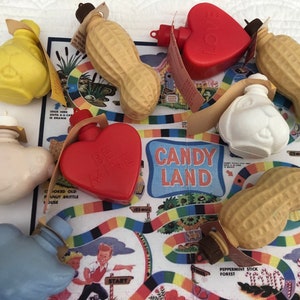以下が含まれることがあります： ピーナッツ、ハート、鳥などの形をした小さなプラスチック製のボトルが10本入った、ビンテージのキャンディーランドゲームボード。ボトルはカラフルな液体で満たされ、小さな栓が付いています。ボードは厚紙製で、カラフルなデザインで、「キャンディーランド」の文字が印刷されています。