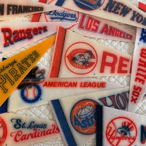 May include: A collection of triangular felt sports pennants featuring various Major League Baseball team names and logos, including San Francisco, New York, Los Angeles, Texas Rangers, Pittsburgh Pirates, Cincinnati Reds, American League, White Sox, St. Louis Cardinals, Houston Astros, and New York Yankees.