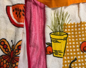 Könnte beinhalten: Ein weißes Küchentuch mit einem roten Wassermelonenmuster, ein rosa Handtuch und ein weißes Handtuch mit einem gelben Topf mit grünen Pflanzen und orangen Kirschen. Die Handtücher sind an einem gelben Stoffband befestigt.