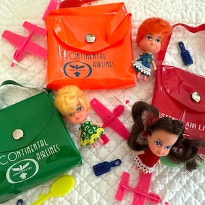 May include: A collection of vintage toy airline sets, including dolls, pink plastic airplanes, and small bags in orange, green, and red. The bags feature the logos of Continental Airlines and Amsterdam Air Lines.