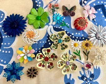 May include: A collection of various floral and butterfly-shaped brooches in diverse colors including blue, green, yellow, red, pink, and white. The pins feature enamel, metal, and painted finishes with intricate petal and wing details.