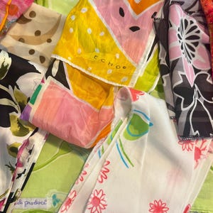 May include: A collection of colorful silk scarves with various patterns. The scarves feature floral, geometric, and abstract designs in shades of pink, yellow, green, and black. Some scarves have the brand name "ECHO" printed on them.