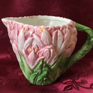 May include: A ceramic creamer or pitcher shaped like a bouquet of pink and green flowers. The pitcher has a white interior and a handle.