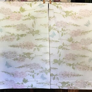 May include: Two white fabric panels with a repeating pattern of pink and lavender floral branches and light blue butterflies. The fabric is held up by wooden clothespins.