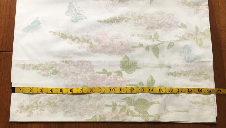 May include: White fabric with a floral and butterfly pattern. The design features pink flowers and green leaves on stems, with light blue and green butterflies. A yellow measuring tape shows a length of 21 inches.