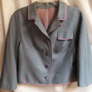 May include: A slate blue cropped jacket featuring a notched collar, three-quarter length sleeves, and four matching buttons down the front. The garment is accented with thin, light pink piping along the collar, front opening, hem, and chest pocket.