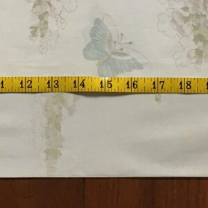 May include: A white fabric with a floral pattern and blue butterfly accents. A yellow measuring tape shows a length of approximately 30 inches. The fabric is likely used for sewing or crafting projects.