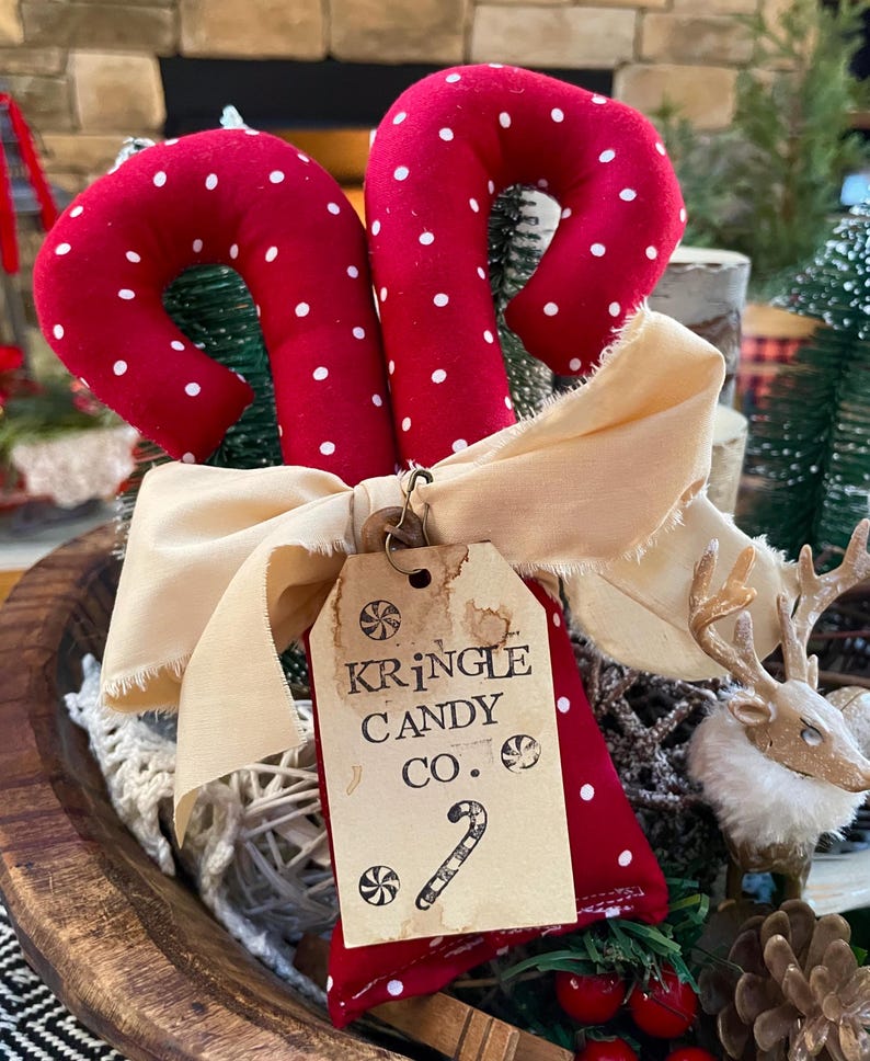 May include: Two red fabric candy canes with white polka dots, tied with a cream-colored bow. A tag reads "Kringle Candy Co." with a candy cane illustration. Festive holiday decor.