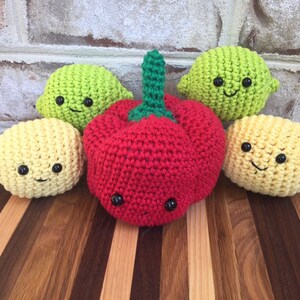 May include: Five crocheted stuffed toys shaped like fruits and vegetables. There are two yellow lemons, one green lime, and one red pepper. All of the toys have black eyes and a smiling mouth.