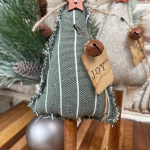 May include: A green and white striped fabric Christmas tree with a wooden star, a bell, and a tag that says "JOY".