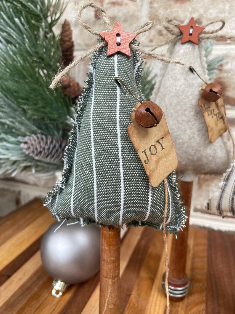 May include: A green and white striped fabric Christmas tree with a wooden star, a bell, and a tag that says "JOY".