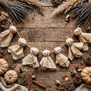 May include: A garland featuring six beige fabric ghost figures strung together on a thin cord. Each ghost is crafted from light-colored cloth with simple black dots for eyes and a mouth, creating a uniform appearance across the entire decorative piece.