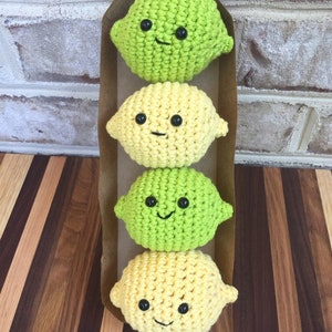 May include: Four crocheted lemon and lime plush toys with smiling faces. The toys are arranged vertically in a brown paper package.