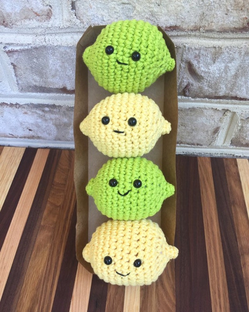 May include: Four crocheted lemon and lime plush toys with smiling faces. The toys are arranged vertically in a brown paper package.
