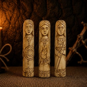 May include: Three cylindrical wooden carvings standing upright, each featuring an engraved figure with long hair and detailed clothing. The left figure holds a circular shield, the center holds a flame, and the right holds a staff. Each base has runes.