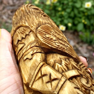 K&ouml;nnte beinhalten: Eine Hand h&auml;lt eine Holzschnitzerei einer Figur mit komplizierten Details. Die Schnitzerei ist in Braun- und Goldt&ouml;nen bemalt und weist ein erhabenes Design auf der Brust der Figur auf.