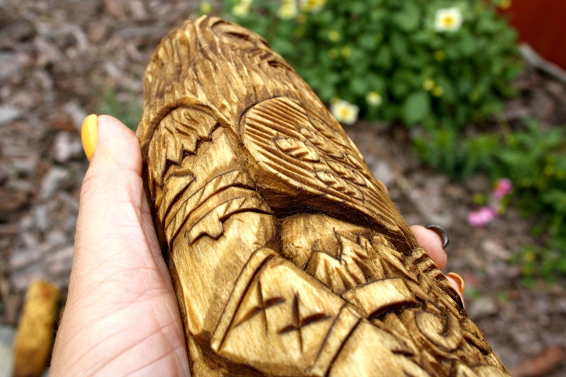 K&ouml;nnte beinhalten: Eine Hand h&auml;lt eine Holzschnitzerei einer Figur mit komplizierten Details. Die Schnitzerei ist in Braun- und Goldt&ouml;nen bemalt und weist ein erhabenes Design auf der Brust der Figur auf.