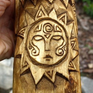 K&ouml;nnte beinhalten: Nahaufnahme einer Holzschnitzerei eines Gesichts in der Sonne. Die Schnitzerei ist detailliert und kunstvoll, mit einem stilisierten Sonnenstrahlendesign und einem Gesicht mit Augen, Nase und Mund.
