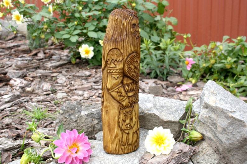 K&ouml;nnte beinhalten: Eine Holzschnitzerei eines nordischen Gottes, m&ouml;glicherweise Odin, mit Bart und einem Wolf zu seinen F&uuml;&szlig;en. Die Schnitzerei ist detailliert und kunstvoll, mit einem Schild und anderen Symbolen, die in das Holz geschnitzt sind.