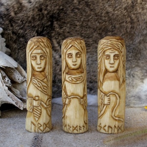 Puede incluir: Tres tallas de madera de mujeres con cabello largo, cada una sosteniendo un objeto en sus manos. Las tallas están etiquetadas como "FRIGG", "NERTHUS" y "SCENCK".