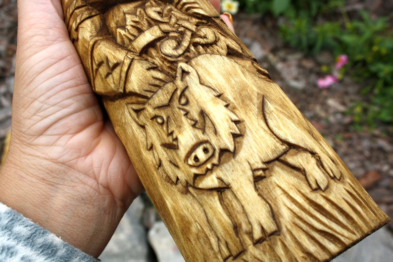 K&ouml;nnte beinhalten: Handgeschnitzte Holzfigur eines nordischen Gottes mit einem Wolf an seiner Seite. Die Figur ist aus hellbraunem Holz gefertigt und hat eine detaillierte Schnitzerei des Gesichts und des Bartes des Gottes. Der Wolf ist ebenfalls detailliert geschnitzt und hat einen grimmigen Ausdruck.