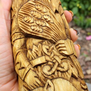 K&ouml;nnte beinhalten: Eine Holzschnitzerei einer Figur, die eine Garbe Weizen h&auml;lt. Die Schnitzerei ist detailliert und kunstvoll, mit einem Fokus auf die H&auml;nde der Figur und den Weizen.