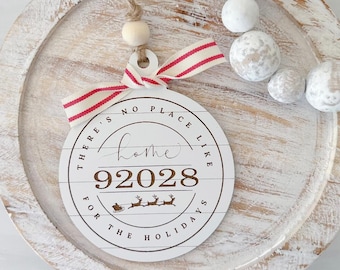 May include: White wooden Christmas ornament with red and white striped ribbon. The ornament has the text "There's no place like home 92028 for the holidays" on it.