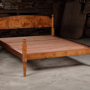May include: A wooden bed frame with a curved headboard and turned posts. The frame is made of maple wood with a natural finish. The bed is designed in a traditional style.