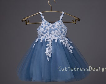 May include: A light blue tulle dress with white lace floral embroidery. The dress has a V-neckline and spaghetti straps. The dress is on a hanger and the brand name "CutiedressDesign" is visible at the bottom of the image.