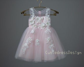 May include: A pink tulle dress with white floral embroidery and a sheer bodice. The dress is on a hanger against a gray background.