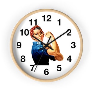 May include: A round wall clock with a light wood frame. The clock face features the iconic Rosie the Riveter image, with black numbers and hands. The woman in the image is wearing a blue shirt and a red and white polka dot bandana.