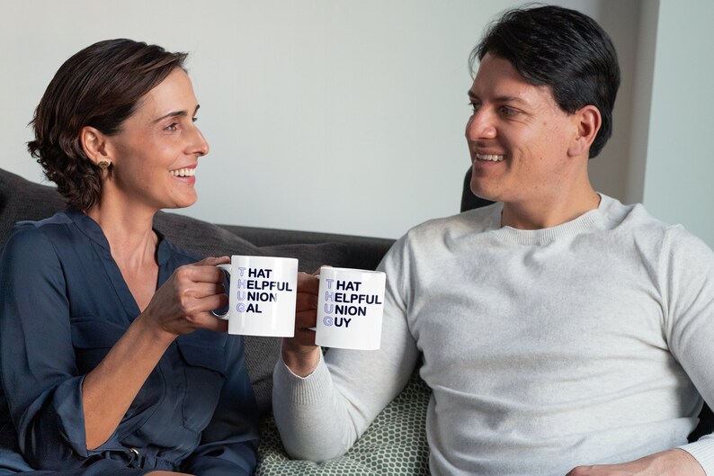 May include: Two people are smiling and holding white mugs with the words "That Helpful Union Gal" and "That Helpful Union Guy" printed on them.