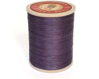 May include: A spool of purple thread with a label that reads "LIN CABLE 100 GR 100% COTON FINE POUR TOUTES SORTES DE BRODERIES".