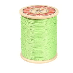 May include: A spool of light green thread. The thread is tightly wound around a wooden spool. The top of the spool has a red and white label with text and a small illustration. The thread is a bright, vibrant green color.