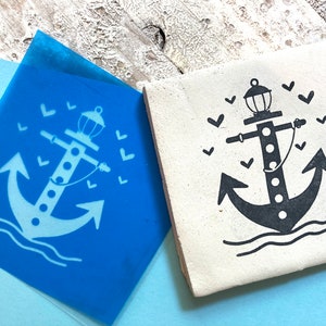 Könnte beinhalten: Ein blauer und weißer Stempel mit Anker- und Leuchtfeuerdesign. Der Anker ist schwarz und das Leuchtfeuer ist weiß. Um Anker und Leuchtfeuer sind kleine weiße Herzen.