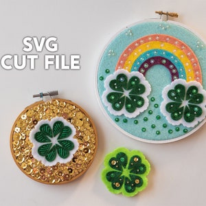 Op de afbeelding: Drie borduurringen met St. Patrick's Day-thema en een klaver. Eén ring heeft gouden pailletten en een klaver, een andere heeft een regenboog en klavers, en de derde is een groene klaver. De tekst "SVG CUT FILE" is zichtbaar.