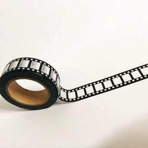 May include: A roll of black and white washi tape with a film strip design. The tape is partially unrolled, showing the design.