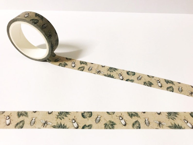 May include: A roll of brown washi tape with a repeating pattern of green leaves and white beetles.