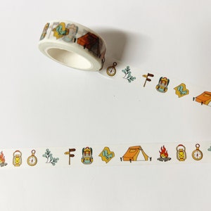 May include: A roll of white washi tape with a repeating pattern of camping-themed illustrations. The illustrations include a tent, a compass, a lantern, a backpack, a campfire, and a tree.