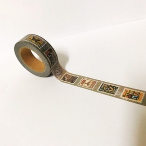 May include: A roll of decorative washi tape featuring a repeating pattern of vintage postage stamps in various colors. The tape is gray with a brown core and is unrolled on a white surface.