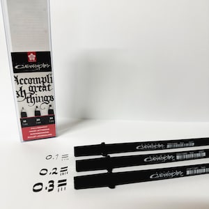May include: Three black calligraphy pens with the brand name "Calligrapher" printed on them. The pens are lined up in a row with the nibs facing the right. The text "0.1", "0.2", and "0.3" is written in black ink below the pens.