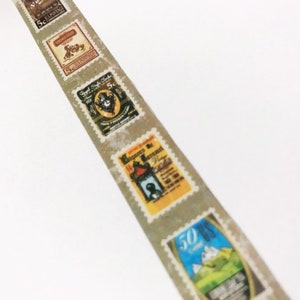 May include: A strip of washi tape featuring vintage postage stamp designs. The stamps are in various colors, including brown, yellow, and blue, with text and illustrations. The tape has a light gray background and a serrated edge.